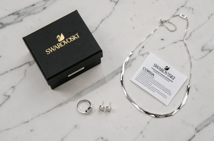 Plat posé de bijoux Swarovski avec boîte d'emballage et carte de garantie sur marbre blanc, illustrant la durabilité et la politique de garantie